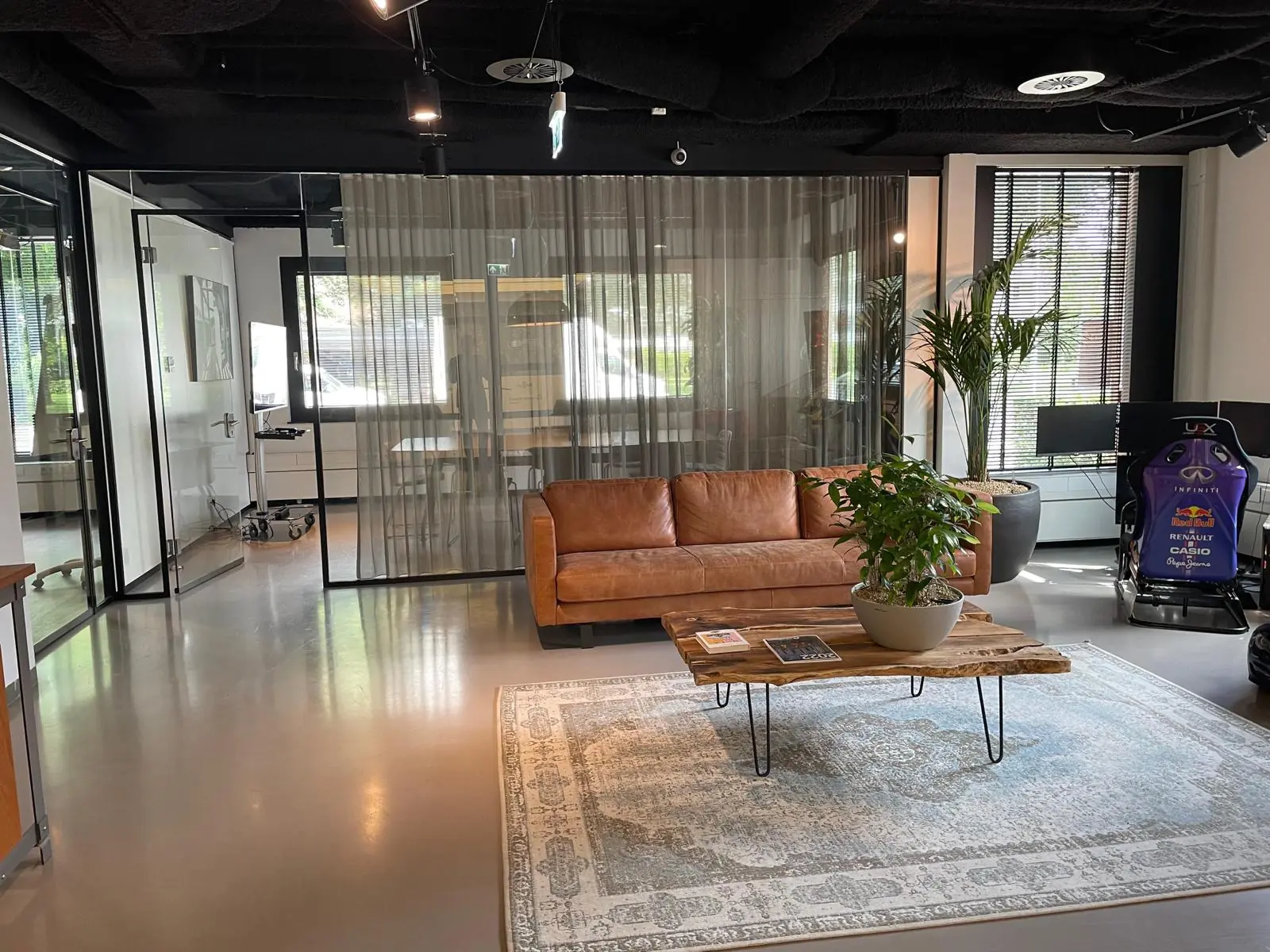 Moderne kantoorruimte aan de De Cuserstraat met een leren bank, houten salontafel, race simulator en glazen vergaderruimtes.